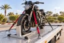 Une moto maintenue par des sangles rouges sur le plateau d’une dépanneuse, roue avant dans un sabot.
