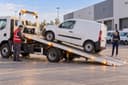 Un utilitaire blanc est chargé sur une dépanneuse dans une zone logistique ; une gestionnaire de flotte observe.