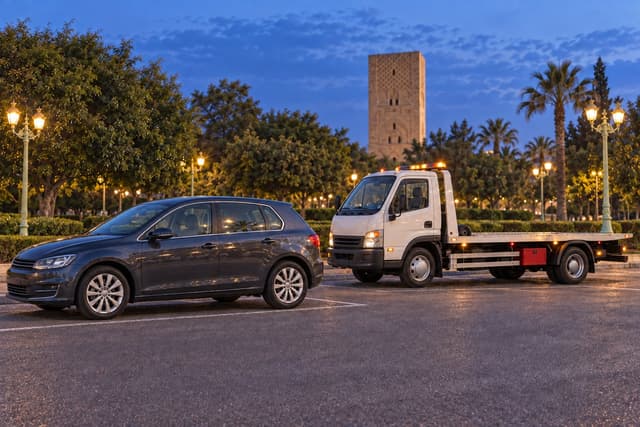Rabat : une voiture et une dépanneuse stationnées près des jardins, la tour Hassan à l’arrière-plan.
