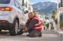 Tétouan : un dépanneur cale la roue d’un SUV dans une rue en pente aux maisons blanches, montagnes du Rif au fond.